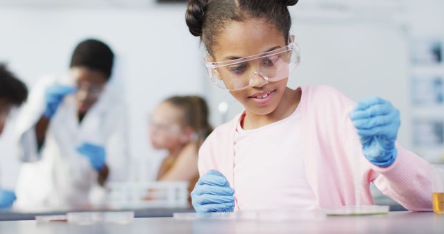 Young African American girl is shown conducting a science experiment in a classroom. She is wearing safety goggles and gloves while working with lab equipment. Ideal for educational materials, science education promotions, classroom activities advertisements, and STEM learning resources.
