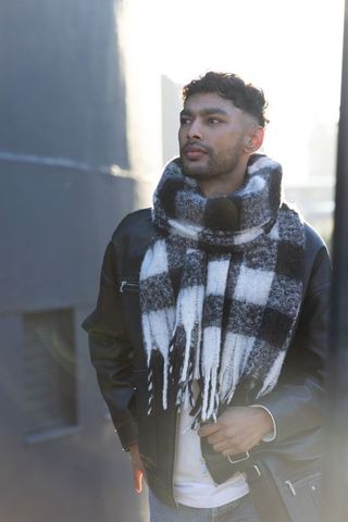 Indian man wearing leather jacket and checkered scarf standing on backlit city street