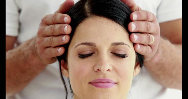 Woman sitting with eyes closed while receiving a head massage. Useful for illustrating concepts of relaxation, wellness, and therapy in advertisements, blogs, and social media content promoting spas and wellness centers. Can also be used in articles related to stress relief and self-care tips.
