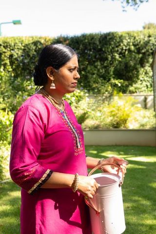 Woman Watering Plants in Vibrant Pink Kurta in Sunny Garden