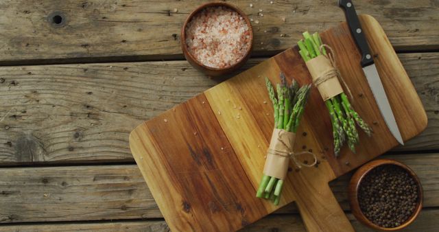 Image of two fresh asparagus bundles on wooden chopping board with knife and salt and pepper. fusion food, fresh vegetables and healthy eating concept.