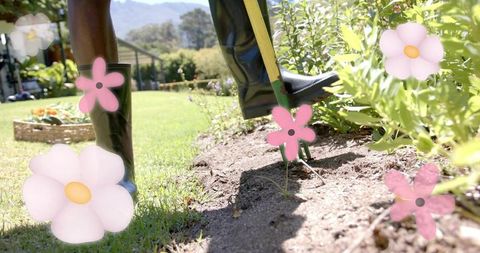 Gardener digging soil with garden fork wearing rubber boots in sunny backyard