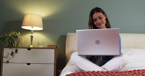 Young woman working on laptop in cozy bedroom, modern home office concept