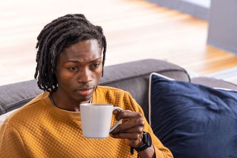 African american man relaxing on sofa holding mug, contemplating morning coffee