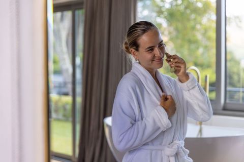 African american woman talking on phone in robe near freestanding bathtub with garden view