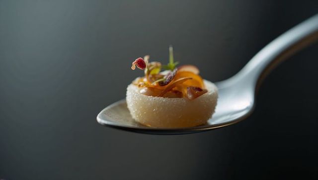 Minimalist gourmet tartlet resting on silver spoon with sugar crystals and microgreens