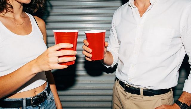 Clinking red cups during casual urban hangout with woman in tank and man in white shirt