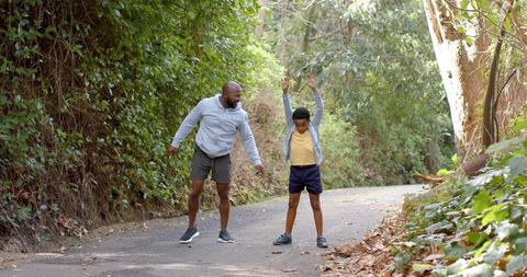 African american father and son stretching on sunlit forest trail exercising together
