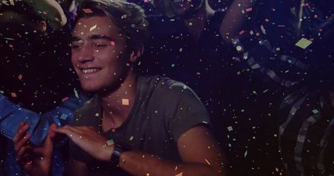 Young man smiling and dancing under multicolor confetti in energetic nightclub crowd