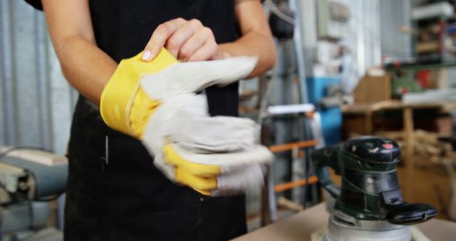 Worker putting on safety gloves in workshop, preparing for manual labor. Can be used in contexts highlighting workplace safety, industrial preparations, or DIY projects.