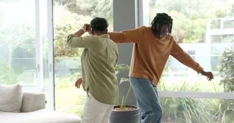African American Couple Dancing and Laughing in Sunlit Modern Living Room with Greenery