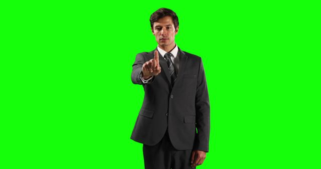 Young adult businessman wearing a formal suit gesturing 'no' with a serious expression. Green screen background allows for easy editing and replacement in various media projects. Useful for presentations, advertisements, and business-related visual content.