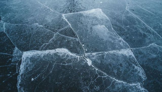 Fractured ice plates forming polygonal floes on frozen lake surface with trapped bubbles