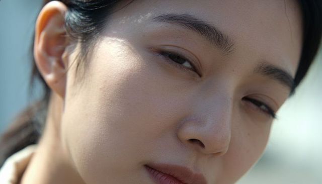 Asian woman squinting close-up in natural light showing skin texture and contemplative gaze