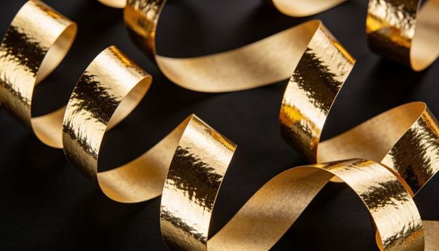 Shimmering gold metallic ribbons curling and catching light in glossy spirals