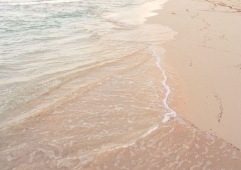 Soft pastel waves lapping pristine pink sand shoreline at golden hour