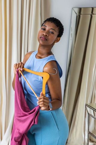 African woman holding wooden hanger with magenta dress in dressing room