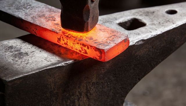 Red-hot steel billet forging on anvil with hammer striking, metalworking workshop detail