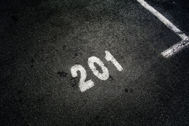 Close-up view of parking spot marked with number 201 on asphalt ground, suitable for illustrating parking facilities or urban infrastructure topics. Good for informational materials about organizing parking areas, urban planning, or transportation logistics.