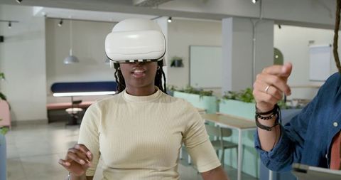 African American Woman Testing VR Headset with Coworker in Bright Open Office