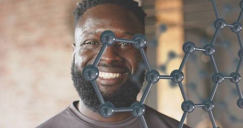 Smiling man wearing crewneck with hexagonal lattice overlay in warm industrial workshop