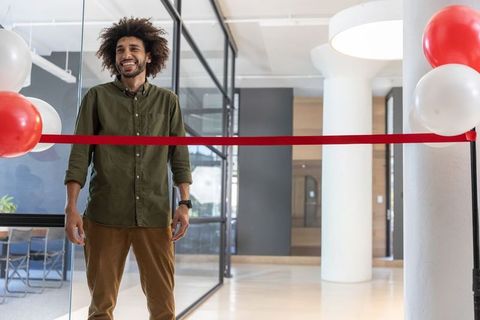 Smiling african american entrepreneur cutting ribbon at modern office grand opening