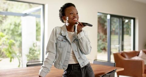 Smiling African American woman speaking into remote in sunlit modern dining room