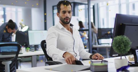 Productive office professional reaching for smartphone at modern open-plan workplace
