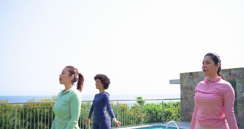 Multicultural women practicing mindful breathing on coastal pool deck during sunrise workout