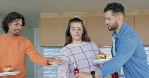Young adults passing plates reaching for bottles at kitchen island serving burgers