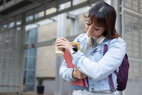 Asian female student studying on campus holding notebooks and coffee, denim jacket