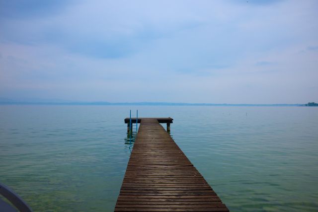 A scenic view of a wooden pier extending into a serene lake under an overcast sky. The calm waters and tranquil atmosphere make this image perfect for promoting relaxation, travel destinations, outdoor retreats, or meditation content. This can also be used in brochures, websites, and social media posts related to nature and tourism.