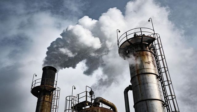 Smokestacks emitting thick smoke with workers on rusted platforms under grey sky