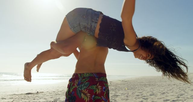 Young couple having fun at the beach, man lifting woman playfully while enjoying sunny day. Perfect for advertising travel, summer vacations, relationships, and joyful outdoor activities.