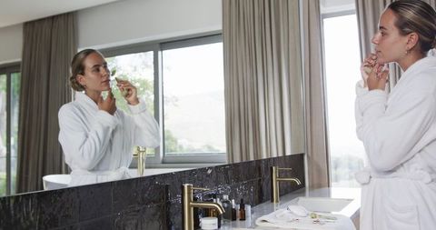 Young woman using facial roller at luxury bathroom vanity in sunlit morning routine