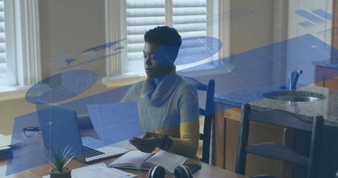 Remote worker reviewing documents at kitchen table with laptop and blue data overlay