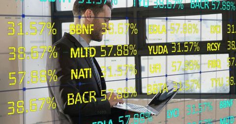 Executive reviewing laptop with financial tickers overlaying modern office windows