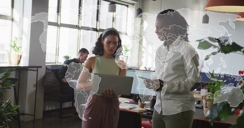 Young diverse coworkers collaborating over laptop in modern open office with global map