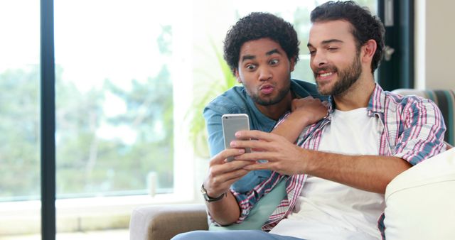 Two young men, one African American and one Caucasian, are looking at a smartphone together, with copy space. Their expressions suggest they are surprised or excited by what they see on the screen.