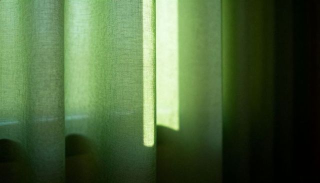 Green sheer curtain filtering sunlight with soft vertical texture and minimalist mood