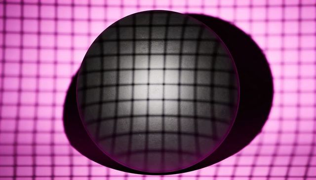 Circular glass lens distorting grid on backlit magenta panel with crescent shadow