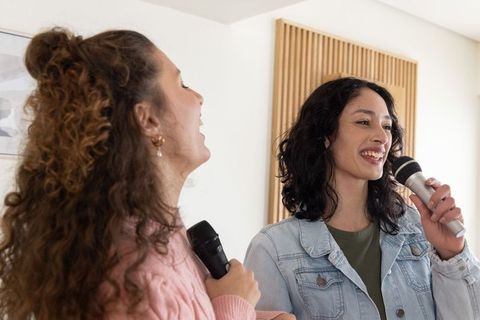 Friends singing together at home using microphones laughing casual karaoke duo