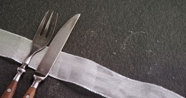 A fork and knife are placed next to each other on a dark textured surface, with copy space. The elegant cutlery setup suggests a fine dining experience or a meal about to be enjoyed.
