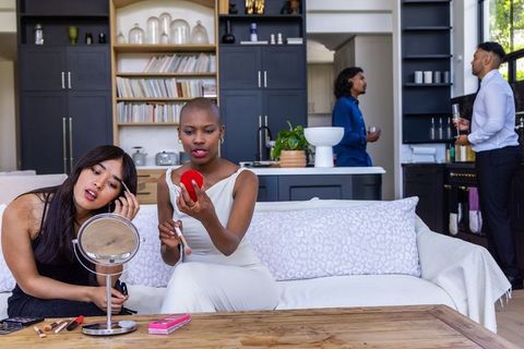 Friends applying makeup on sofa in stylish open-plan living space preparing for night out