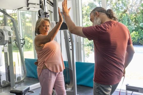 Senior woman and trainer high-fiving during home gym workout, resistance band training