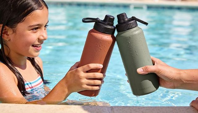 Smiling girl clinking insulated water bottles poolside on sunny day, summer hydration lifestyle