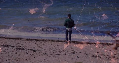Man standing on beach facing ocean with geometric network overlay