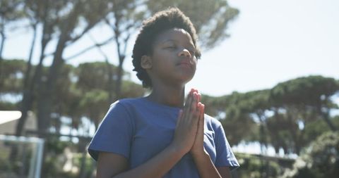 Praying woman outdoors with eyes closed and hands clasped in meditation and reflection