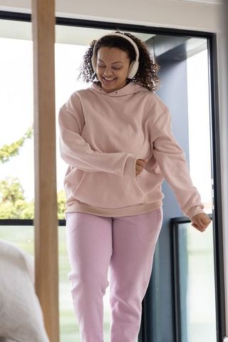 Joyful woman dancing in pastel loungewear with wireless headphones on balcony