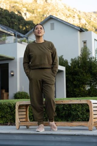 Mid adult asian woman standing on poolside ledge wearing olive joggers and sneakers